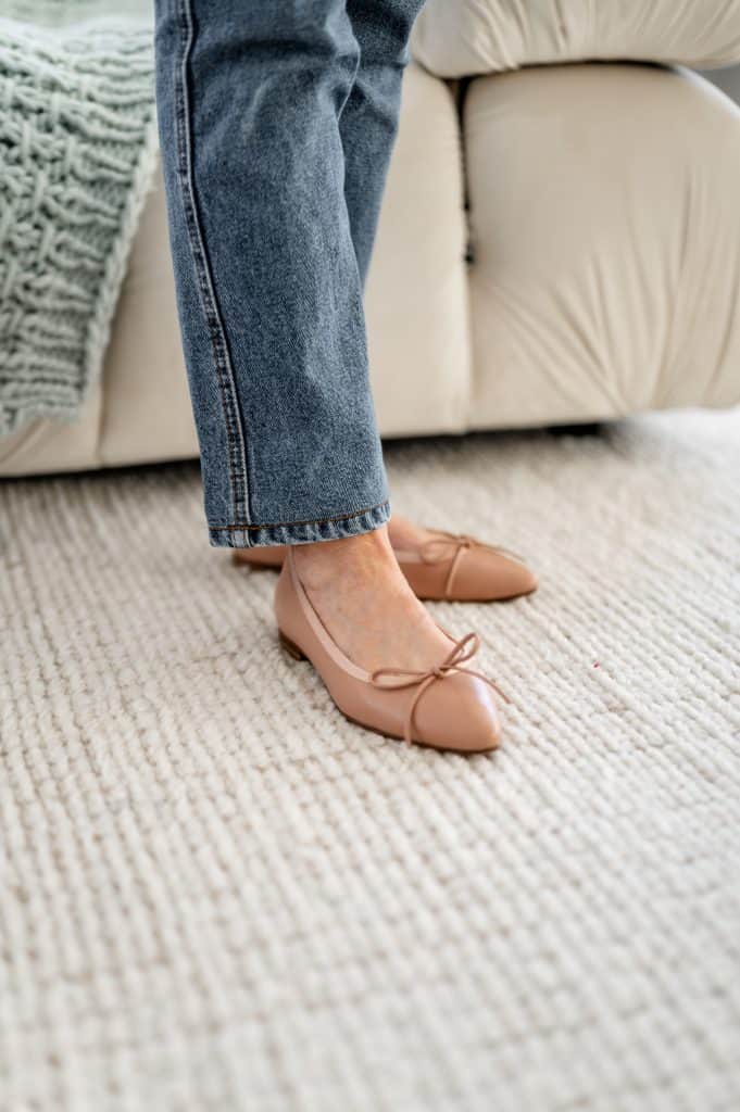 woman stading on an off white carpet wearing nude pointy toe comfortable flats and ankle length jeans