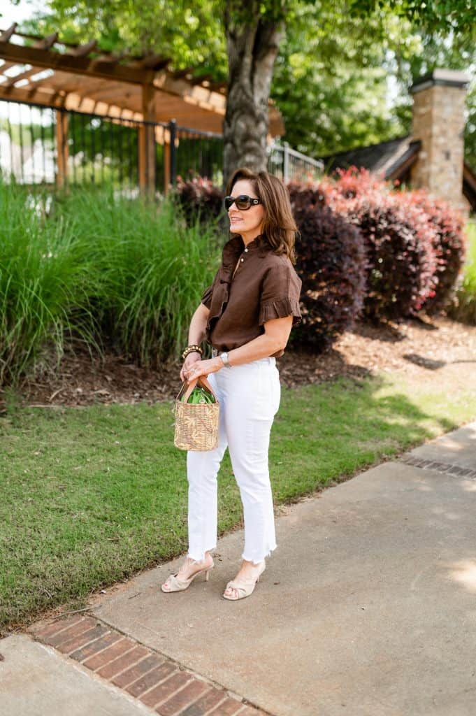 petite woman wearing white jeans for petites stright leg style with a brown top standing in front of a park