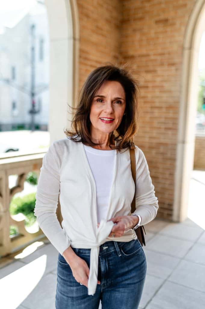 brunette woman standing in an open air portico wearing a short cardigan sweater and jeans, a type of lightwieght spring jackets