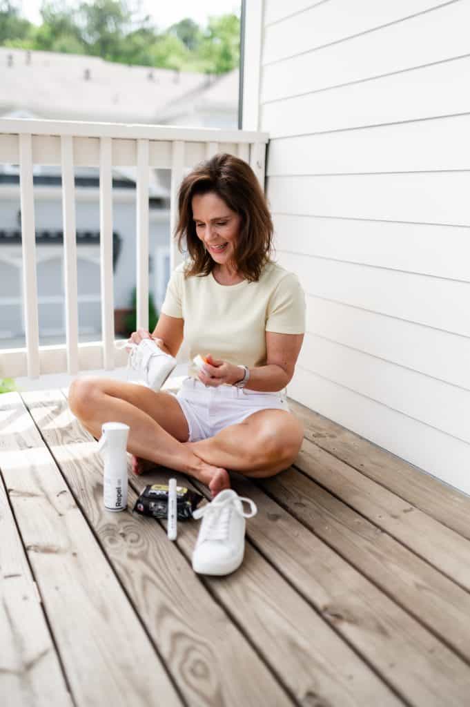 woman sitting on a wooden porch floor to clean white sneakers