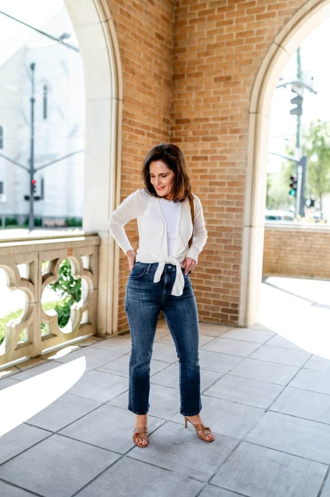 brunette woman wearing a white short cardigan, jeans, and cognac heeled sandals