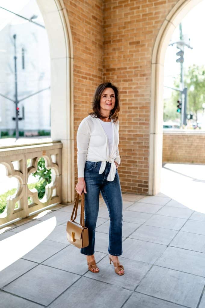 petite brunette woman standing in an open air porch wearing a lightweight spring jacket and jeans