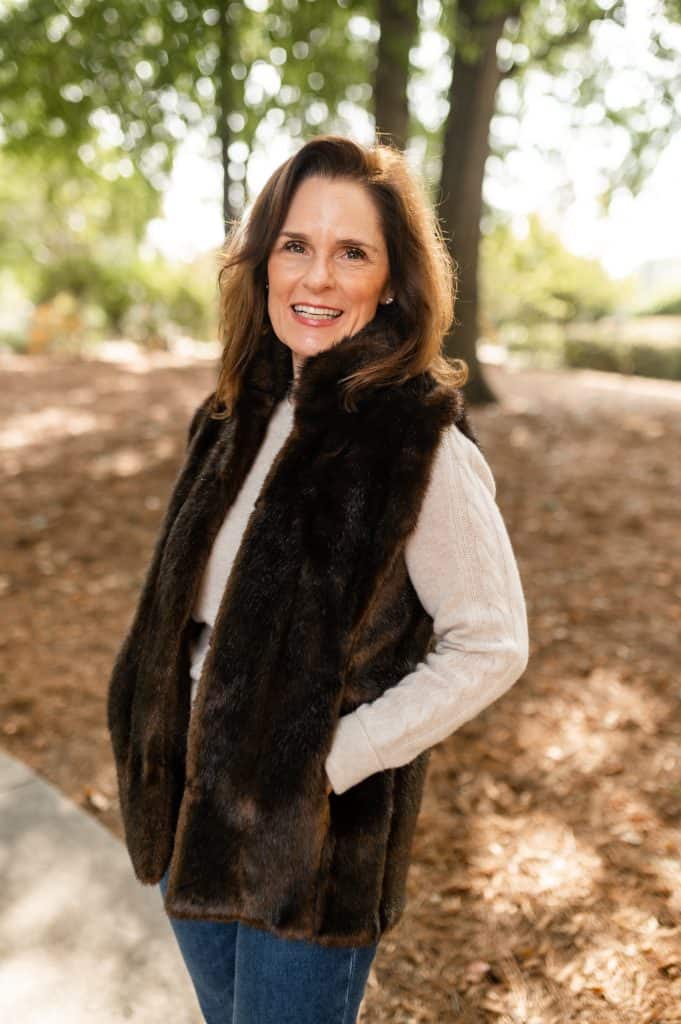 brunette woman wearing an oatmeal sweater and a brown faux fur vest, brown faux fur is a fall fashion trend for 2024