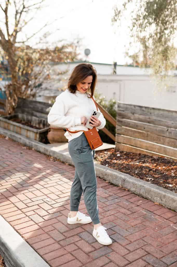 petite brunette woman wearing an ivory sweatshirt green joggers and veja retro sneakers