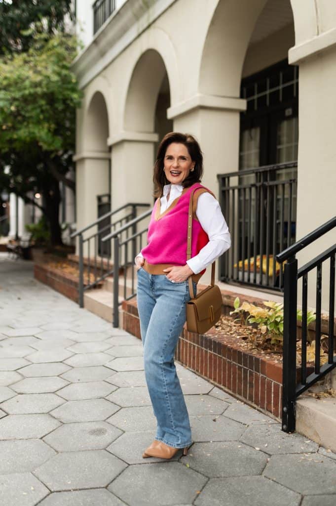 brunette woman wearing a white shirt, pink sweater vest, jeans and camel boots