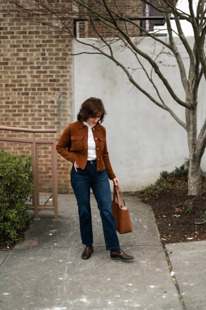 Cropped jeans hitting at the ankle on a petite woman styled with a cardigan and loafers.