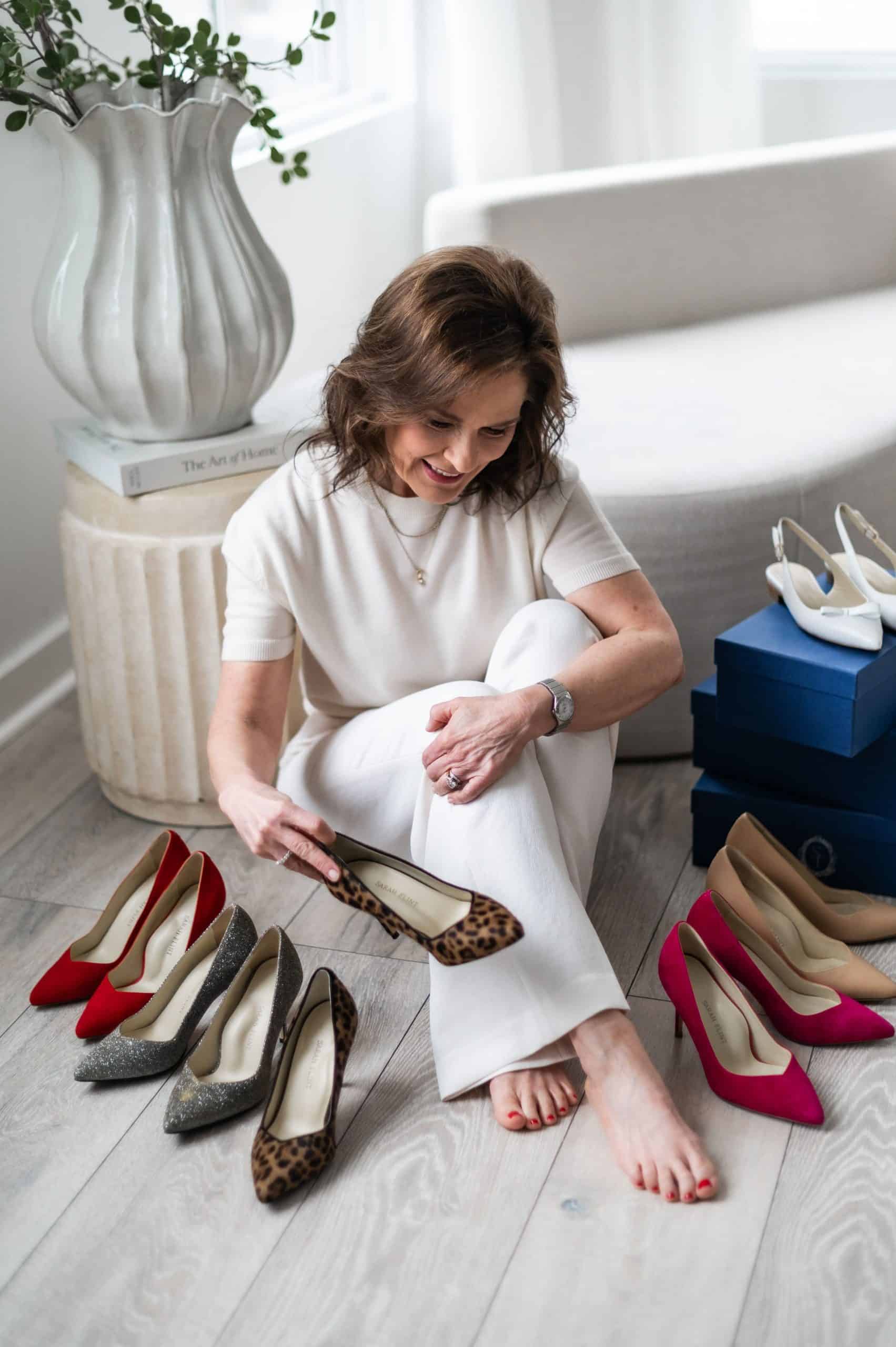 Beth Ferguson sitting on the floor surrounded by multiple pairs of Sarah Flint Perfect Pump 85 heels in leopard, red, nude, pink, and metallic.